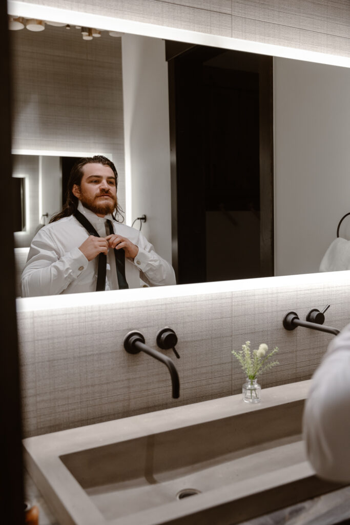 Groom putting his tie on while getting ready at the Airbnb on his elopement day.