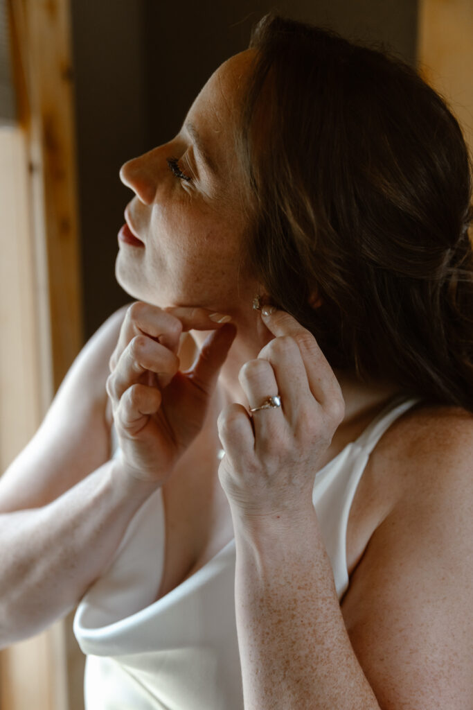 A bride putting her earrings on while getting ready for her elopement. 