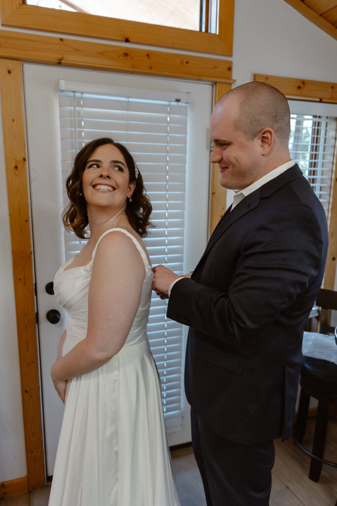 A groom helping his bride get into her dress at their elopement in Estes Park, Colorado. 